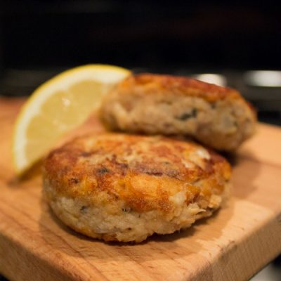 Pan fried canned salmon shaped into small patties with a lemon wedge nearby.
