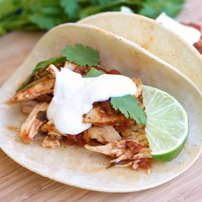 Tortillas filled with shredded chicken breast mixed with salsa, topped with sour cream with a lime wedge.