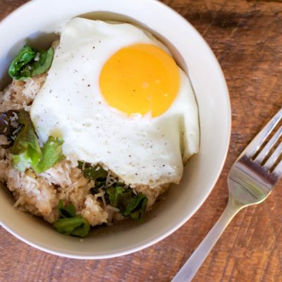 Bowl of oatmeal mixed with cooked spinach with a sunny fried side up egg.