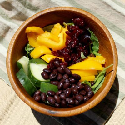Bowl of neatly placed black beans, chopped yellow pepper, cucumber, and spinach.