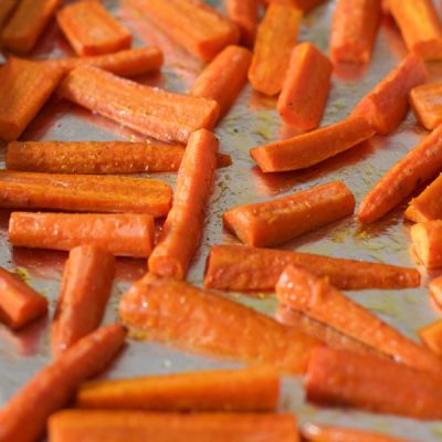 Roasted carrots cut into long slices spread on a cookie sheet.