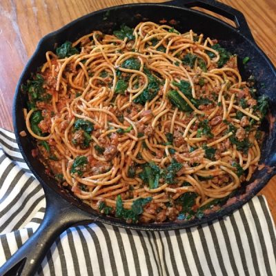 Skillet of whole wheat spaghetti mixed with ground beef, onion, chopped spinach, topped with shredded mozzarella cheese.