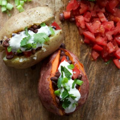 Sliced open baked potato filled with black beans, diced tomatoes, and topped with basil sprigs.