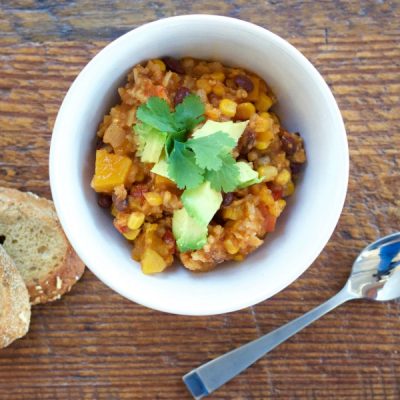 Bowl of chili made with black beans, bell pepper, onions, carrots, squash, corn, tomatoes, barley, zucchini, kale, and garlic, topped with chili powder