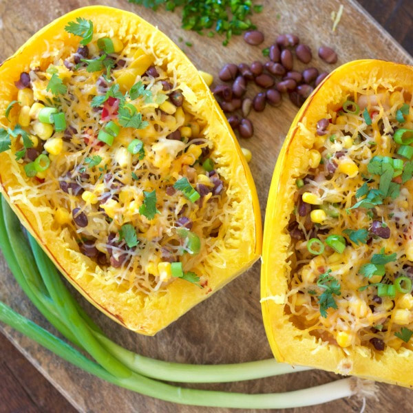 Cooked halved and hollowed spaghetti squash stuffed with black beans, corn, peppers, onion, and salsa topped with shredded cheese.