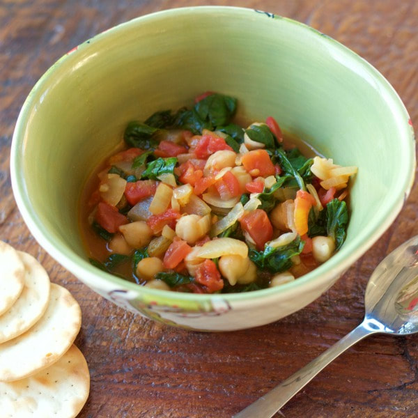 Bowl of boiled chickpeas mixed with onions, diced tomatoes, chopped spinach, and golden raisins.