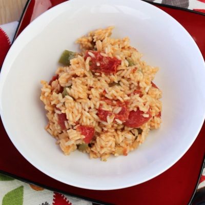 Bowl of Spanish rice mixed with chopped green and red peppers.