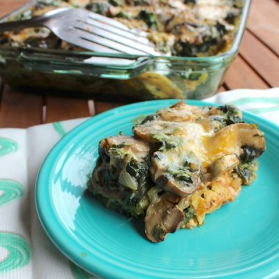Slice of a casserole of spinach, onion, peppers and mushrooms topped with enchilada sauce and melted cheese.