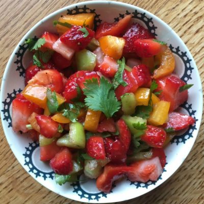 Bowl of chopped strawberries, red onion, red, orange, and green pepper topped with a sprig of basil.