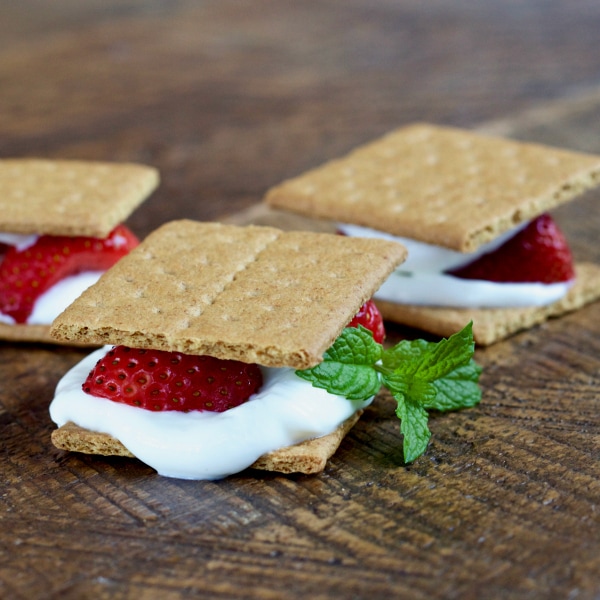 Two graham cracker sandwich stuffed with yogurt, strawberries, and a sprig of basil.