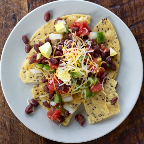 Plate of tortilla chips topped with red beans, chopped summer squash, tomatoes, sprinkled with shredded cheese.