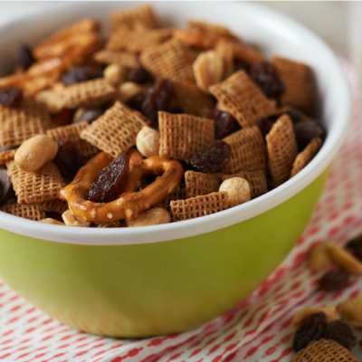 Bowl of mixed sweet and salty diced mix trail with Chex cereal, cheerios, peanuts, pretzels, and raisins.