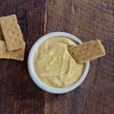 Bowl of pumpkin puree mixed with yogurt and cream cheese with a graham cracker dipped into it.