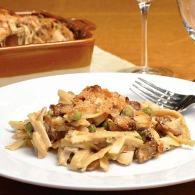 Plate of fettuccine pasta mixed with mushrooms, chopped tomatoes, chopped turkey, topped with parmesan cheese.