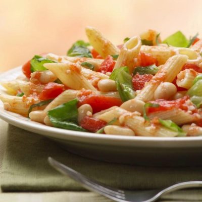 Plate of penne pasta mixed with cannellini beans, chopped fresh basil leaves and chopped tomatoes.