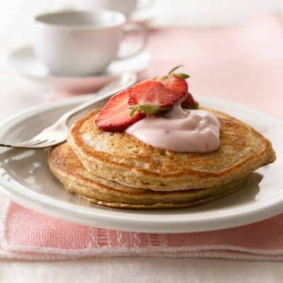 Plate of pancakes cooked with yogurt, topped with strawberry yogurt and sliced strawberries.