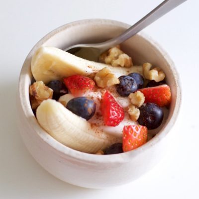 Bowl of halved bananas mixed with blueberries, strawberries and granola, covered in yogurt.