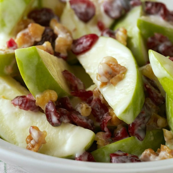 Bowl of apple wedges topped with dried cranberries, walnuts, and yogurt.