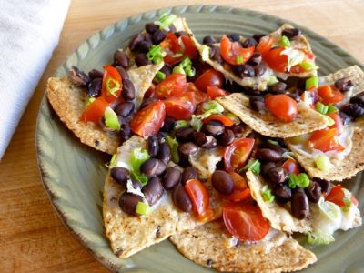 plate full of nachos topped with black beans, melted cheese, and diced veggies