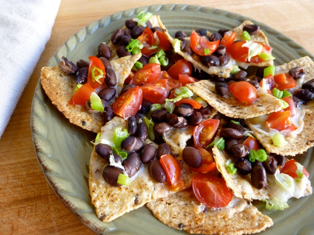 plate full of nachos topped with black beans, melted cheese, and diced veggies