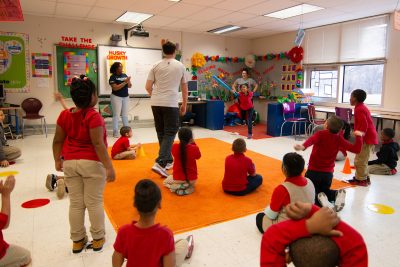 Kids playing a modified version of baseball in the classroom. Student swings a bat while the rest of the class is in the field or on the bases.